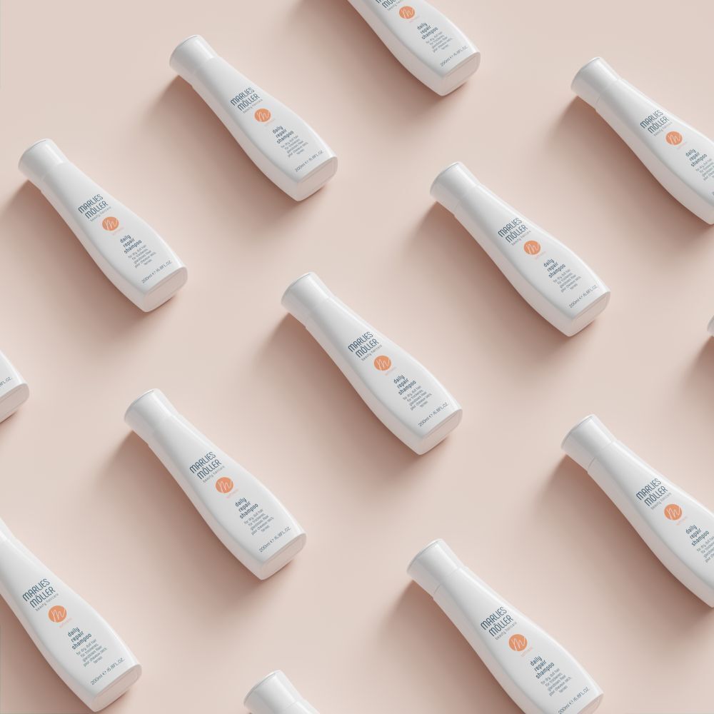 Mehrere weiße Flaschen mit Klappverschluss. Aufschrift: Marlies Möller, daily repair shampoo. Auf rosa Hintergrund.