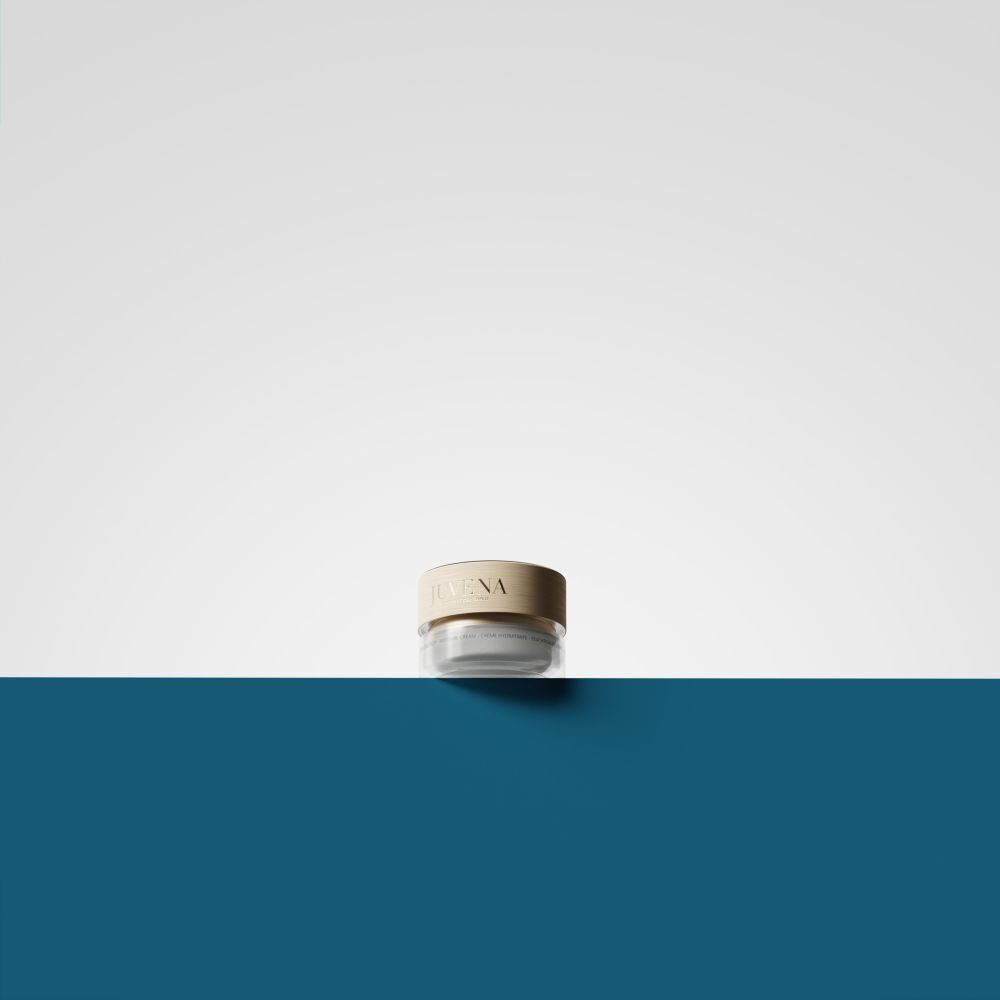 Un pot de crème avec couvercle doré. Inscription: JUVENA. Le pot est posé sur une surface bleue.