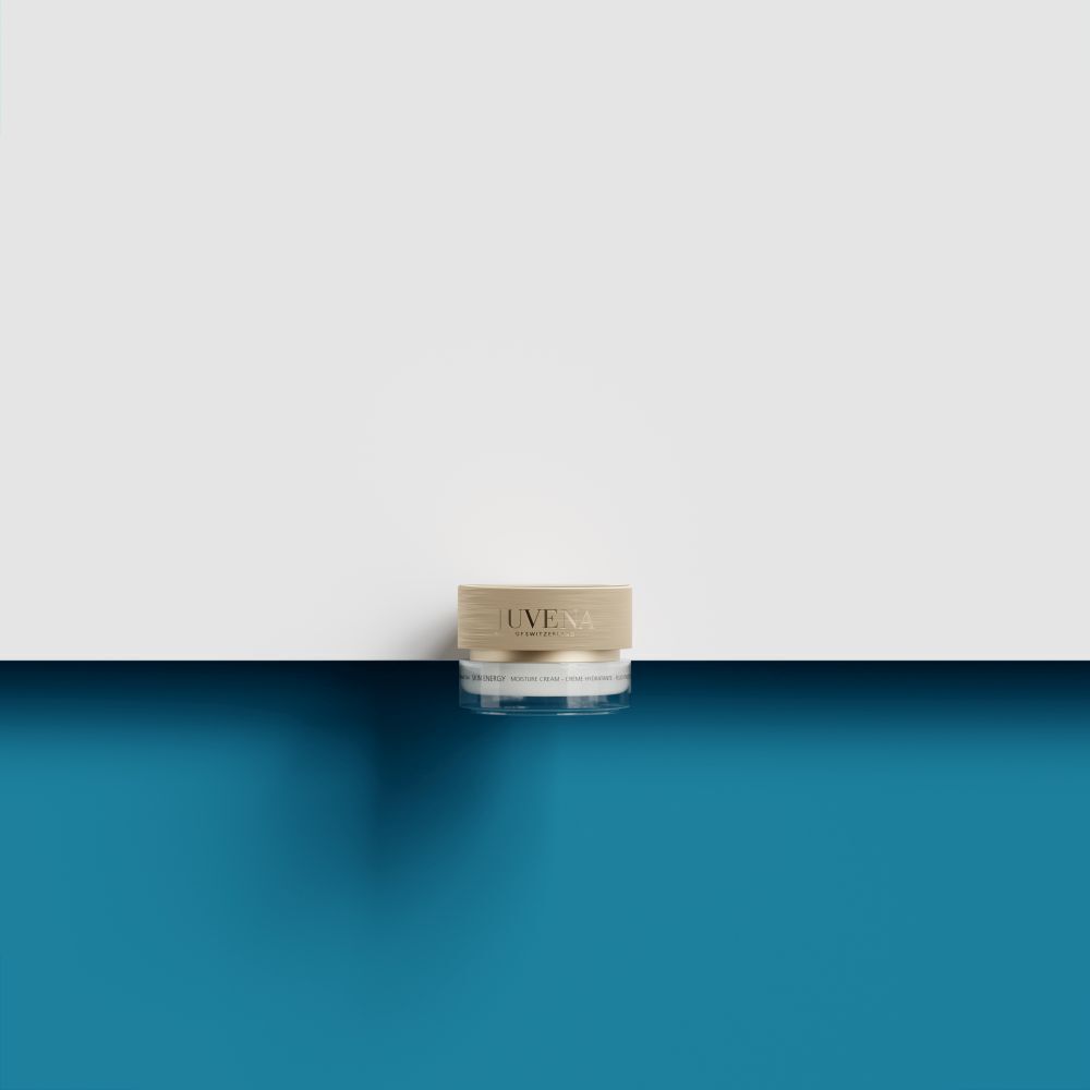 Pot avec couvercle doré. Inscription : JUVENA. Pot transparent. Posé sur fond bleu et blanc.