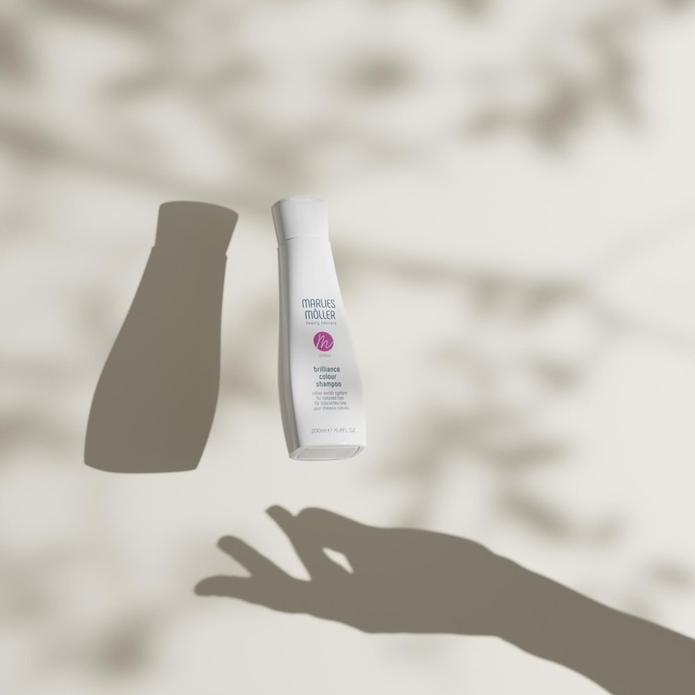 Weiße Shampoo-Flasche und Schatten auf hellem Hintergrund. Aufschrift: Marlies Möller, Brilliance Colour Shampoo. Für coloriertes Haar.