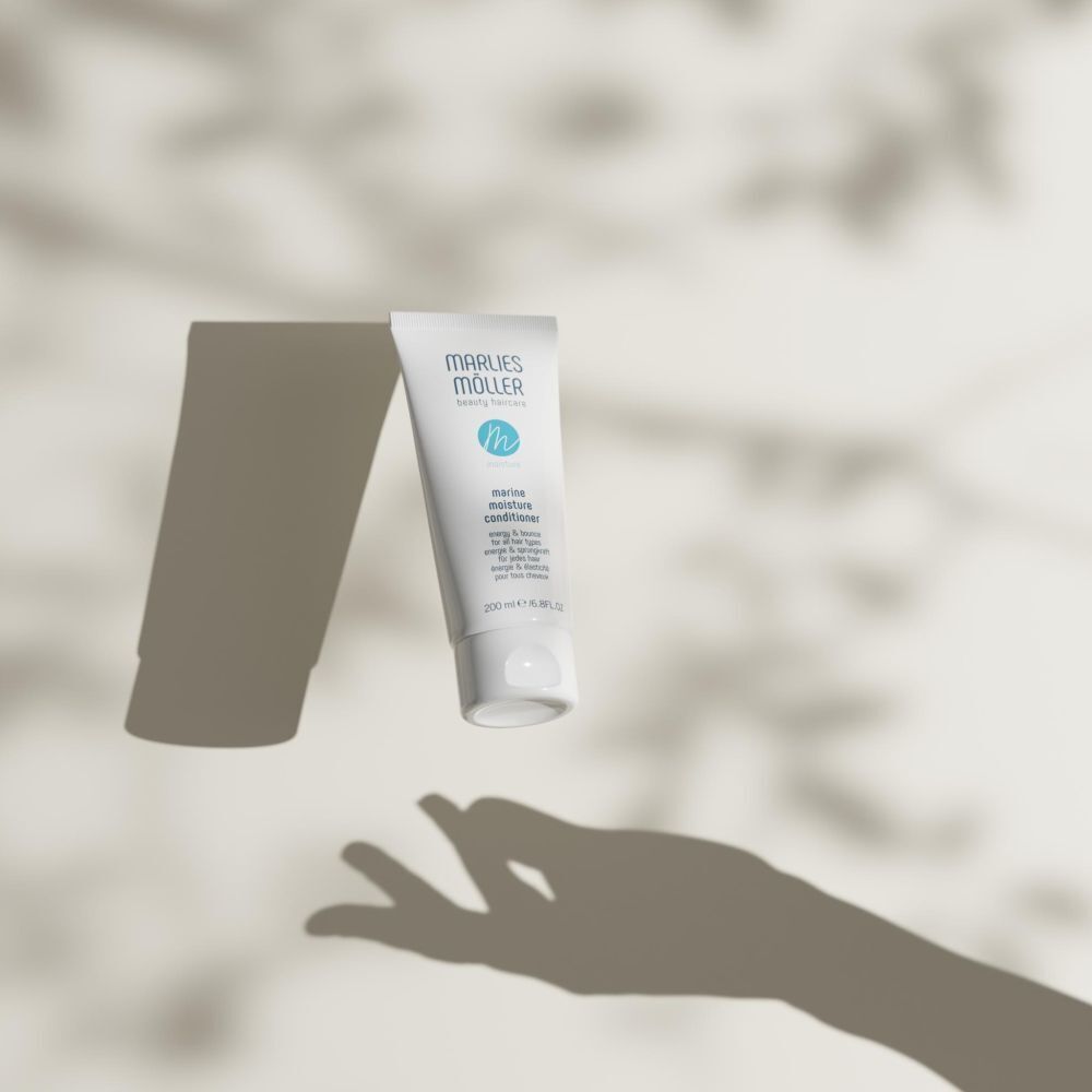 Eine Tube Marlies Möller Marine Moisture Conditioner schwebt vor einem Hintergrund mit Schatten.
