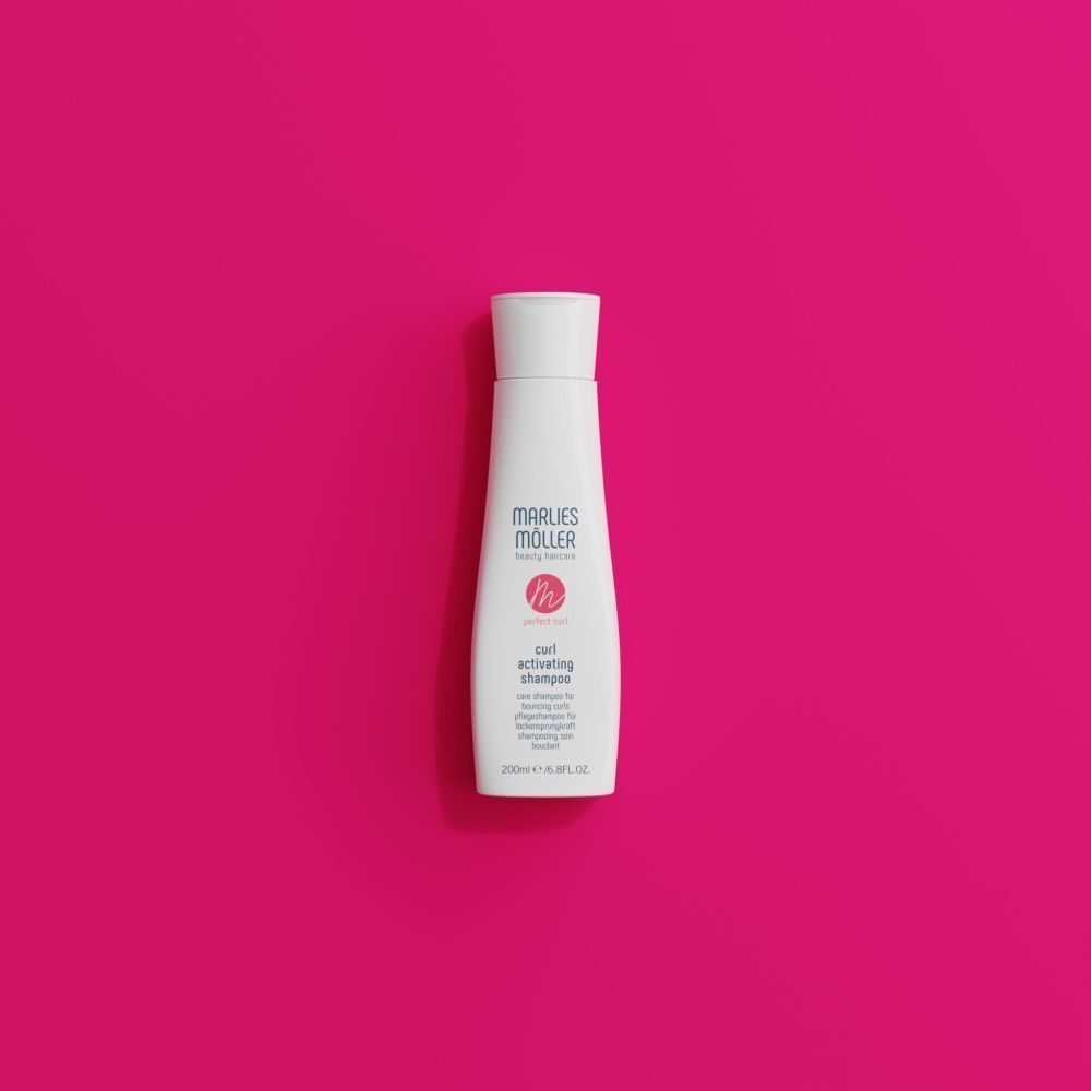 Marlies Möller Curl Activating Lotion in weißer Flasche auf pinkem Hintergrund.