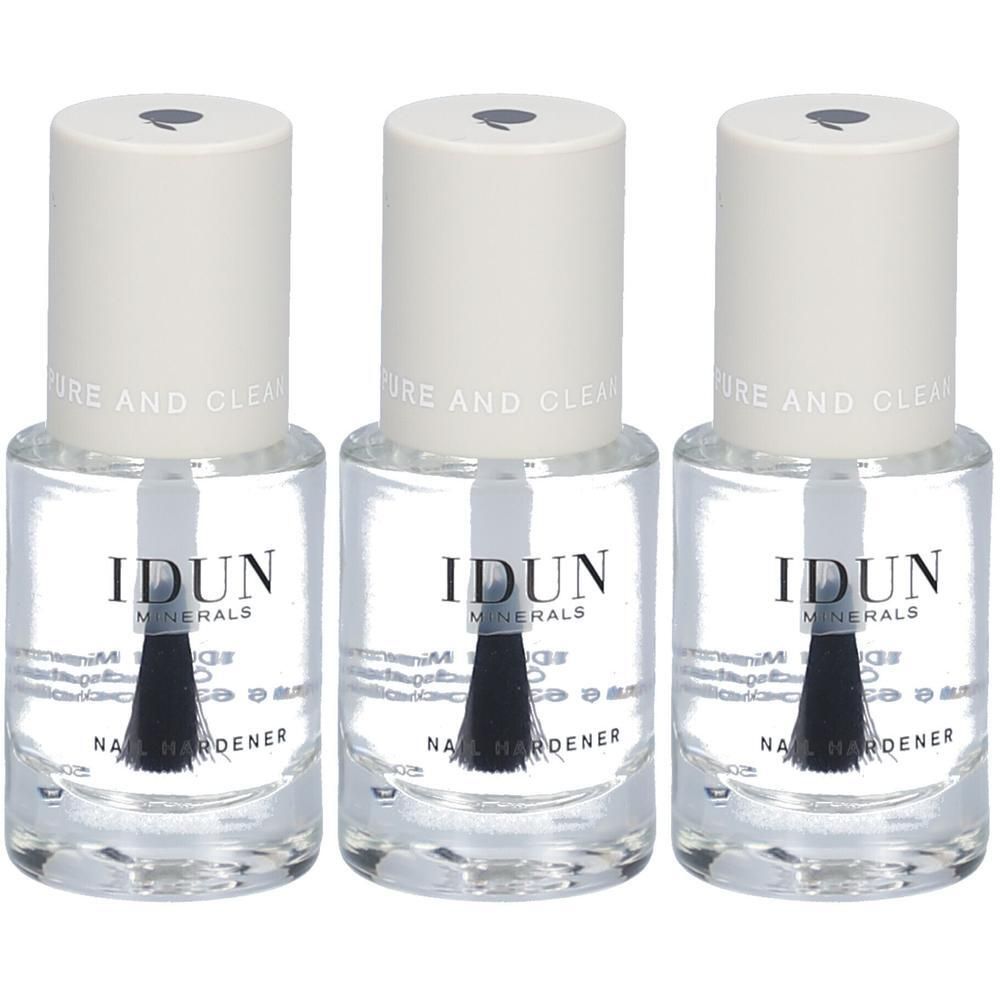 Trois flacons de durcisseur pour ongles IDUN Minerals. Liquide clair dans des flacons en verre avec des bouchons blancs. Pinceaux noirs visibles.