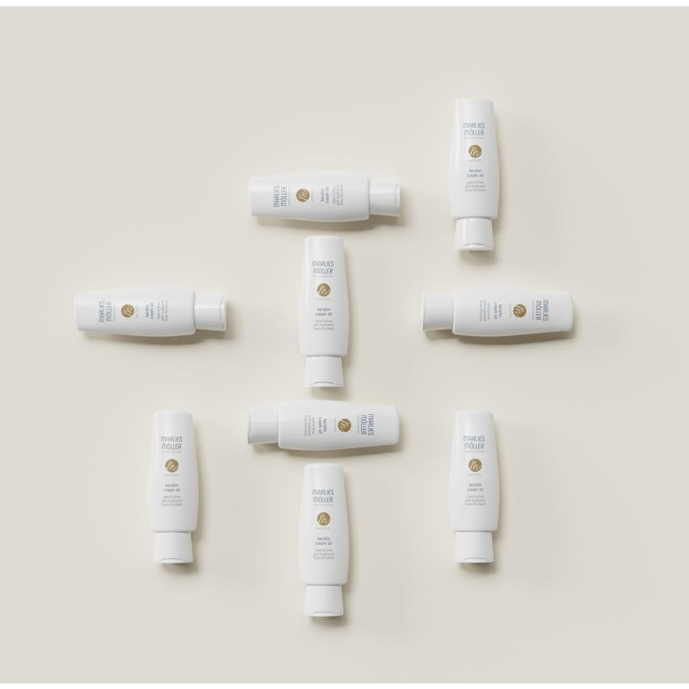 Plusieurs flacons blancs Marlies Möller Keratin Cream Oil Sleek & Shine disposés sur une surface claire.