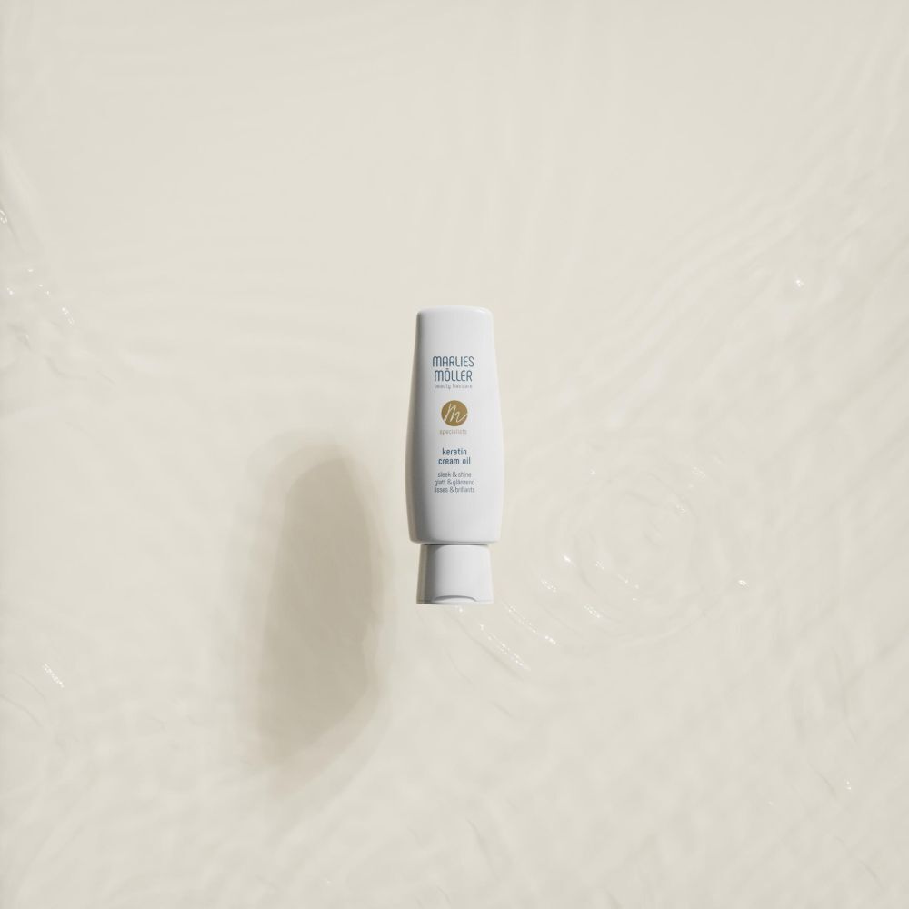 Un flacon blanc Marlies Möller Specialist Keratin Cream Oil Sleek & Shine dans l'eau.