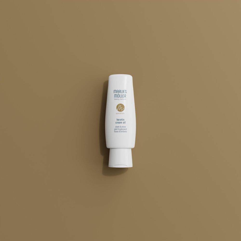 Un flacon blanc Marlies Möller Specialist Keratin Cream Oil Sleek & Shine sur fond brun.
