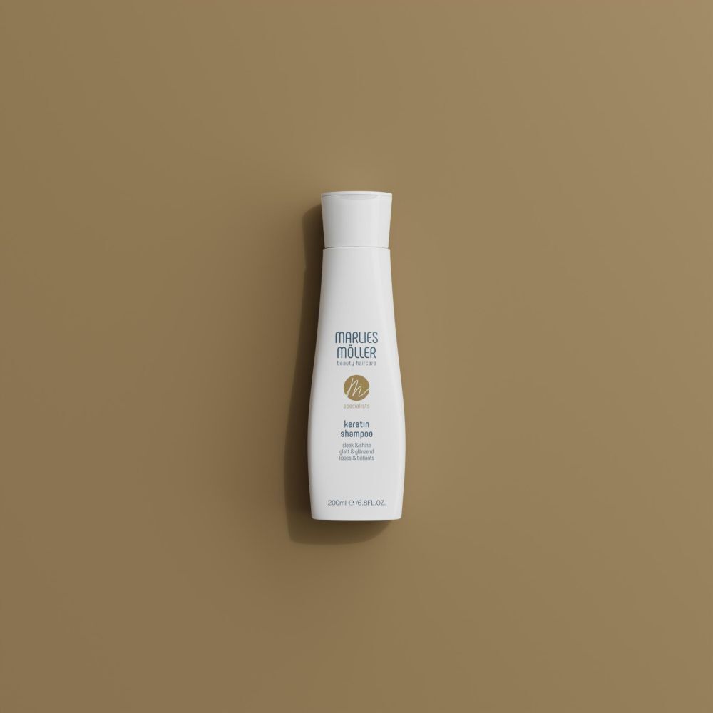 Eine weiße Flasche Marlies Möller Keratin Shampoo Sleek & Shine auf einem braunen Hintergrund.