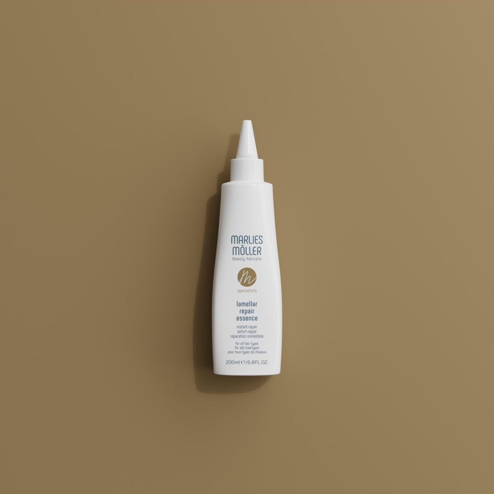 Un flacon blanc Marlies Möller Lamellar Repair Essence sur fond brun.