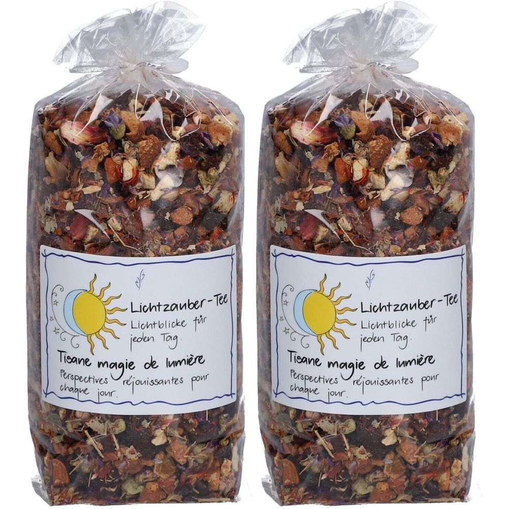 Zwei Beutel Kräutertee. Klare Plastikverpackung. Etikett mit Text: Lichtzauber-Tee, Tisane magie de lumière. Sonnen- und Mond-Illustration.
