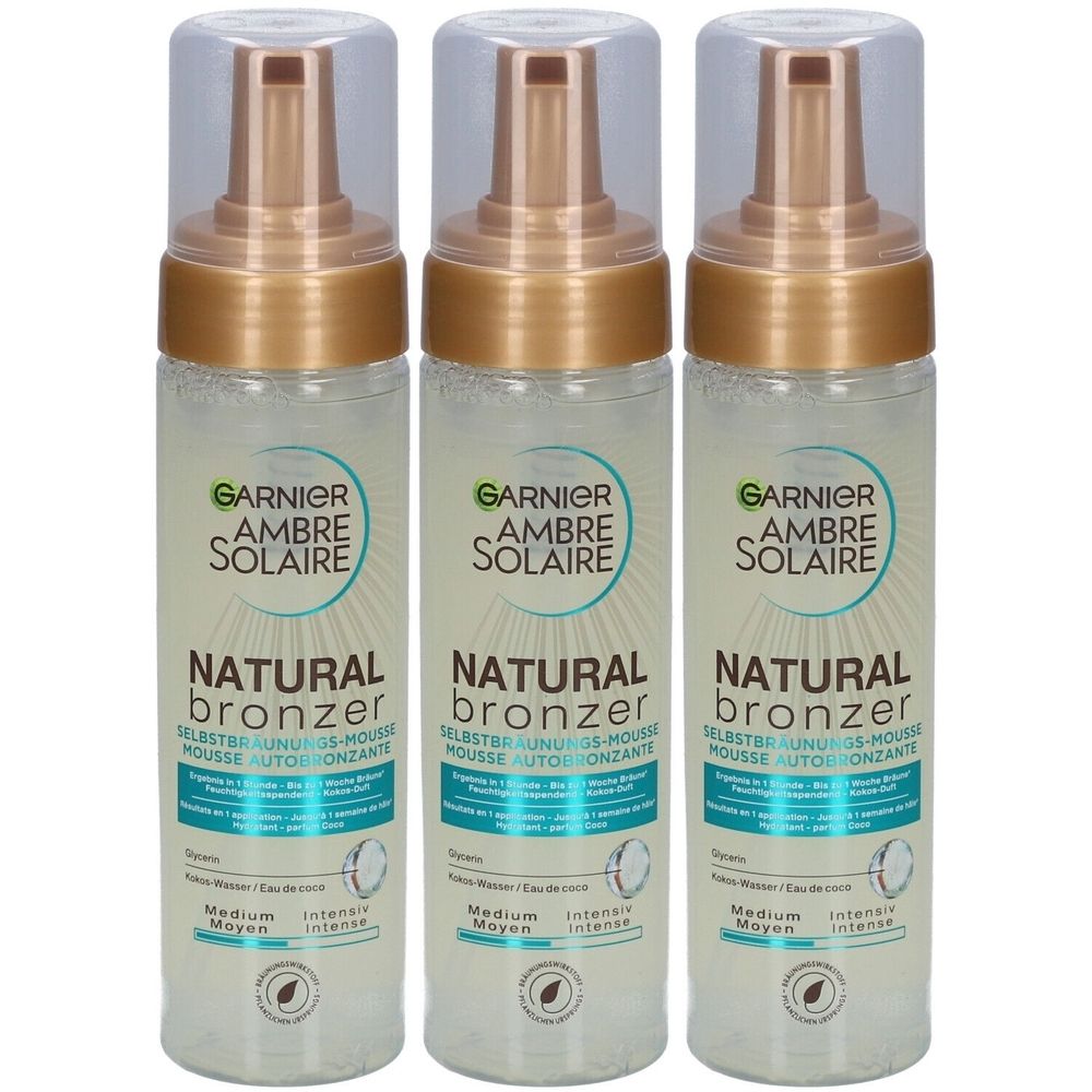 Trois flacons de mousse autobronzante Garnier Ambre Solaire Natural Bronzer. Flacons transparents avec pompes et bouchons dorés.