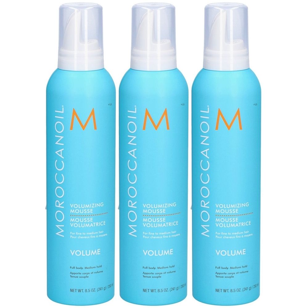 Trois flacons bleus avec vaporisateur blanc. Inscription: MOROCCANOIL, VOLUMIZING MOUSSE, VOLUME. Logo 'M' orange.