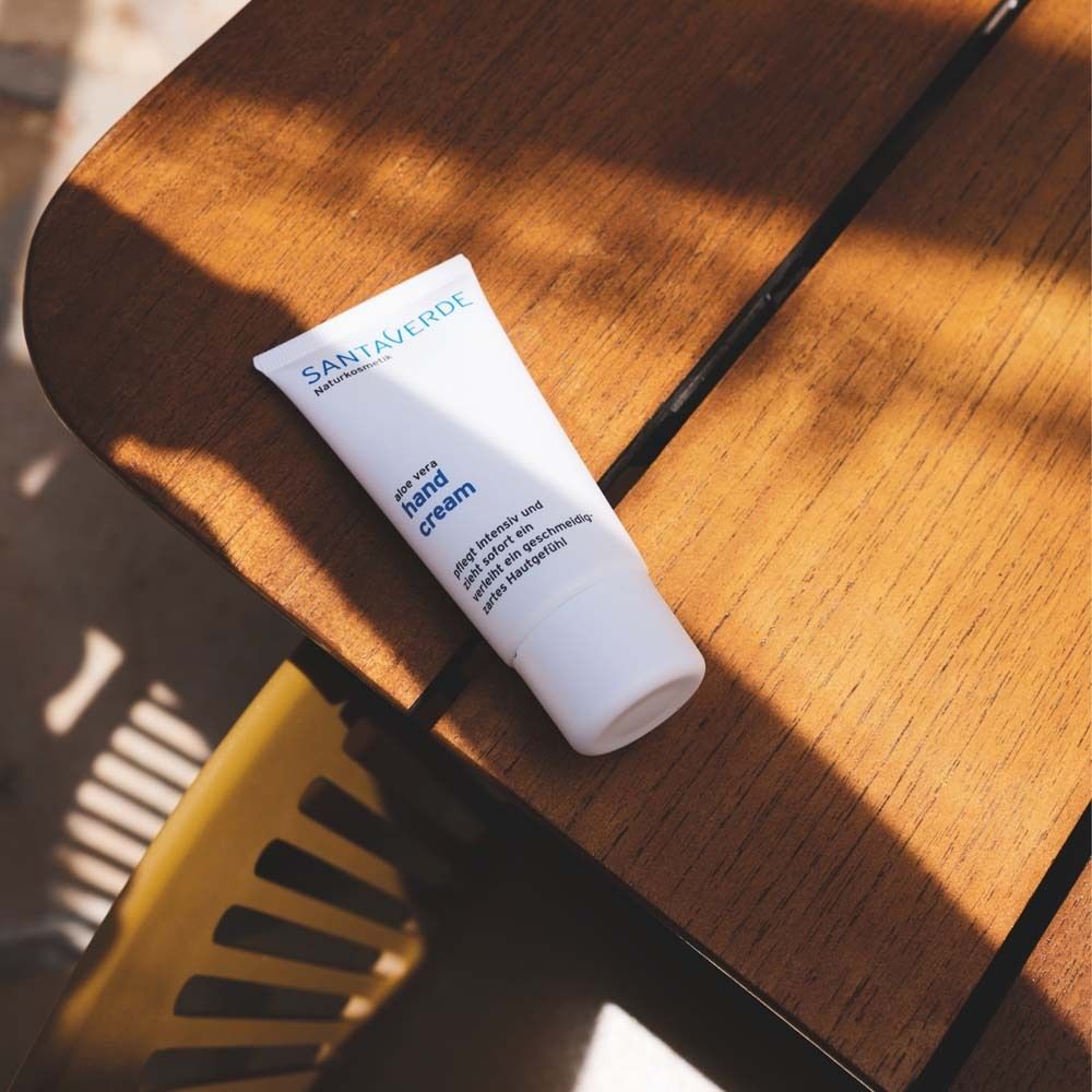 Weiße Tube SANTAVERDE Handcreme auf Holzoberfläche. Produktname und Text: hand cream. Teilweise im Schatten.