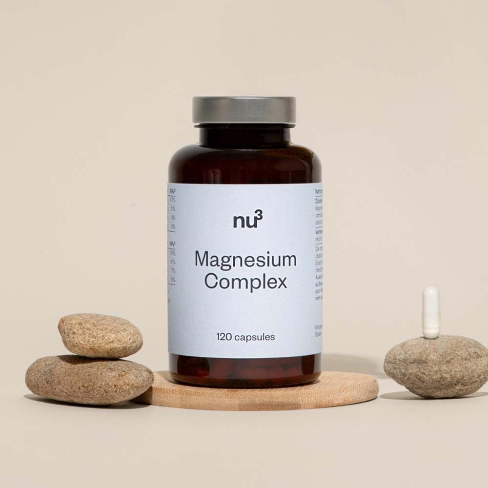 Braune Flasche mit weißem Etikett. Aufschrift: Magnesium Complex, 120 Kapseln. Dekoration mit Steinen.