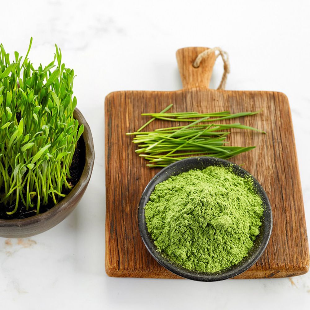 Herbe de blé verte, poudre et brins frais sur planche de bois. Dans des bols et sur une planche. Fond : marbre blanc.