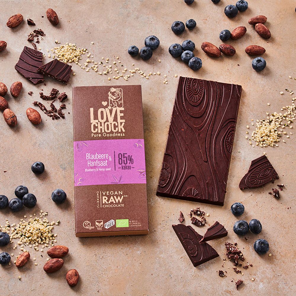 Schokoladentafel und zerbrochene Stücke, Blaubeeren, Kakaobohnen und Hanfsamen. LOVECHOCK-Verpackung.