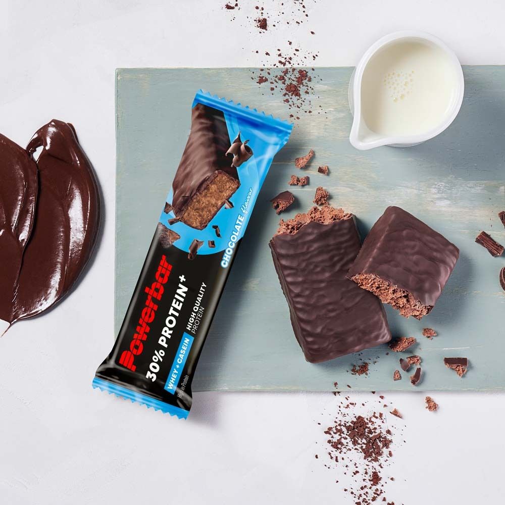 Proteinriegel und zerbrochene Stücke. Aufschrift Powerbar, 30% Protein+, Whey+Casein, High Quality Protein, Chocolate flavour. Milchkanne.