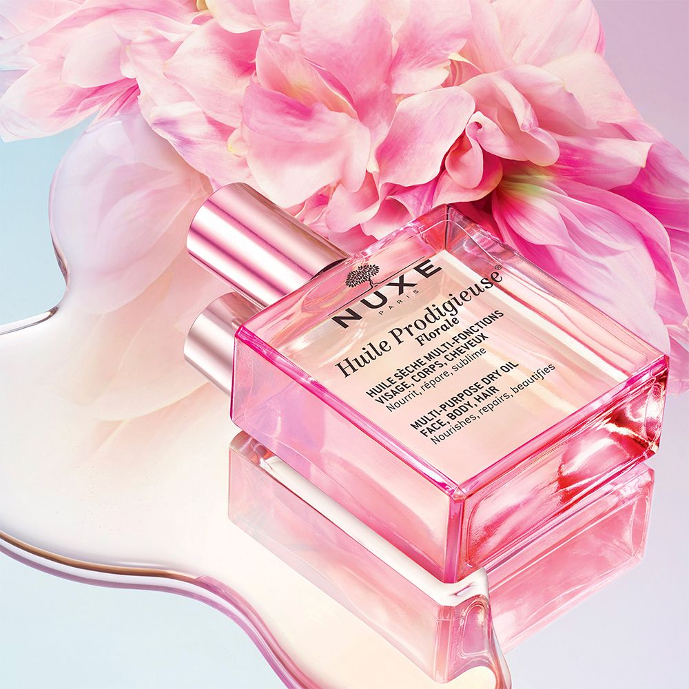Un flacon carré avec liquide rose, entouré de fleurs roses. Inscription : NUXE Huile Prodigieuse® Floral.
