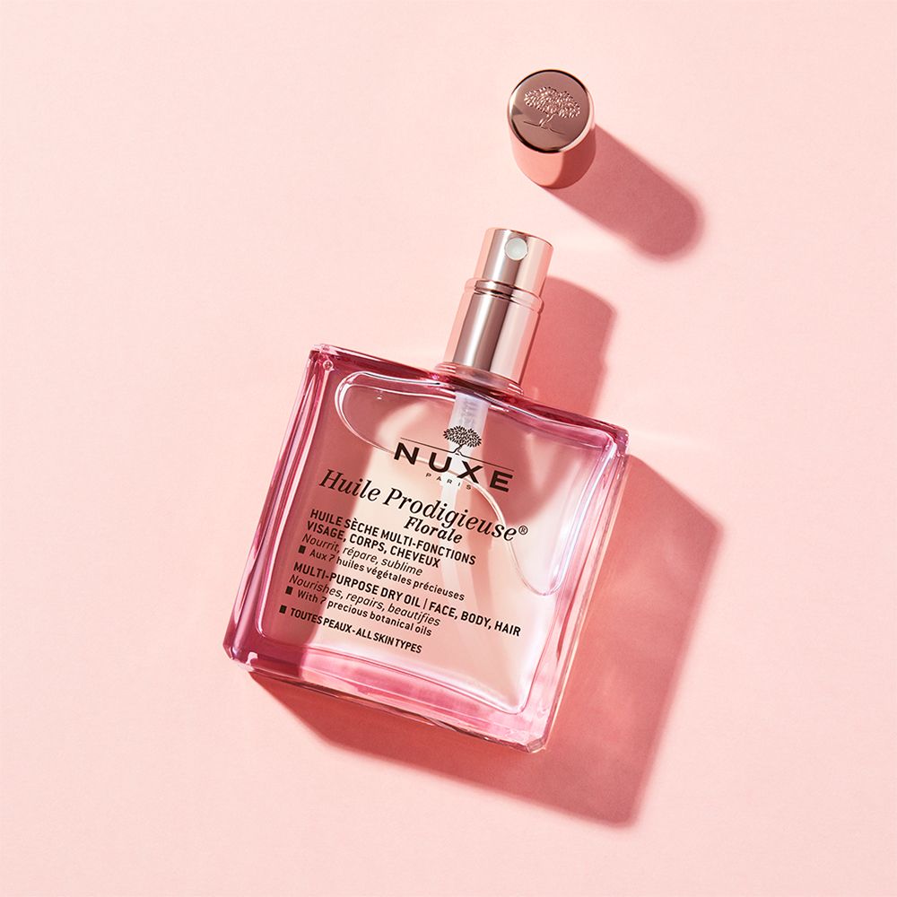 Un flacon carré avec liquide rose et bouchon doré. Bouchon à côté. Inscription : NUXE Huile Prodigieuse® Floral.