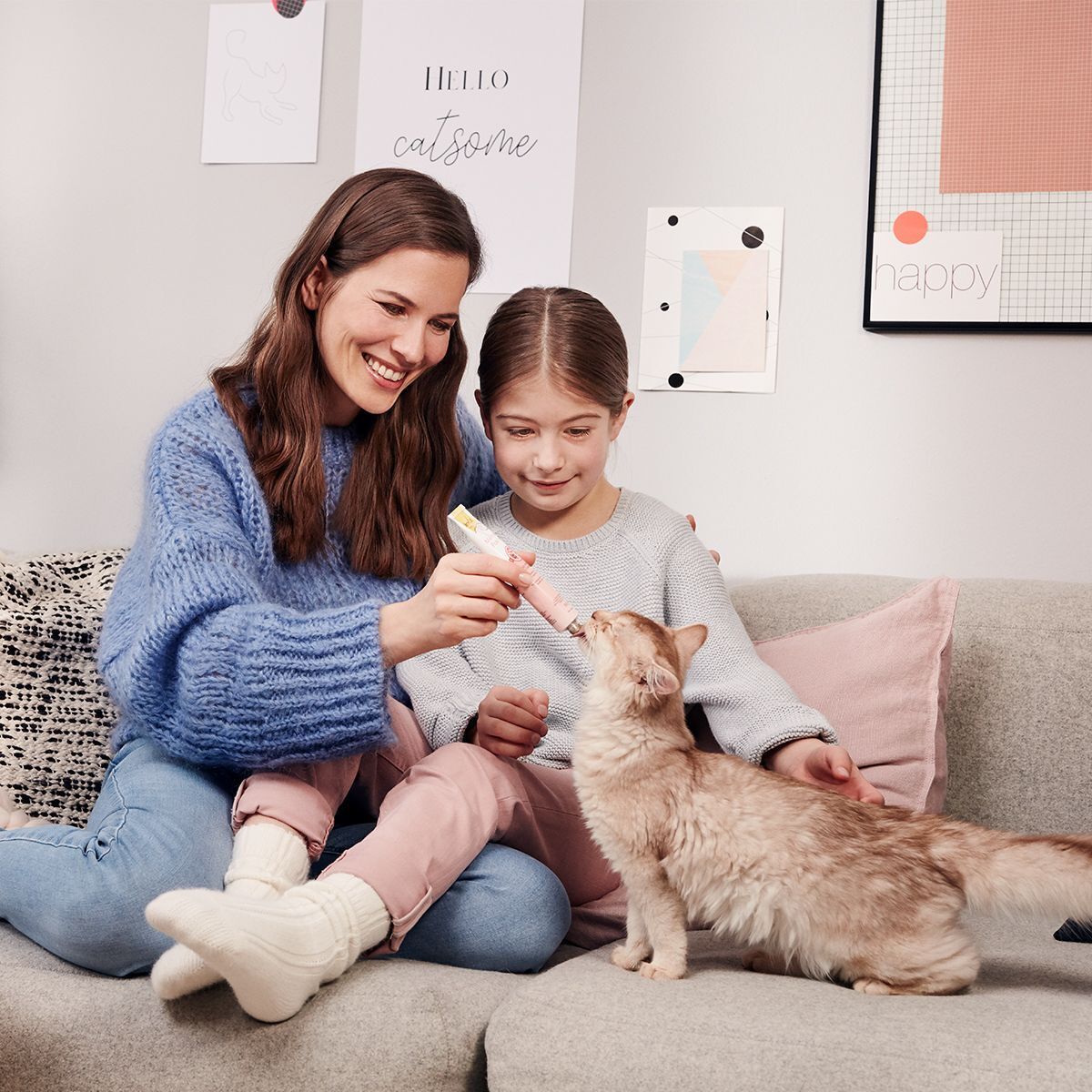 Frau und Kind füttern Katze mit GimCat Multi-Vitamin Paste Extra.