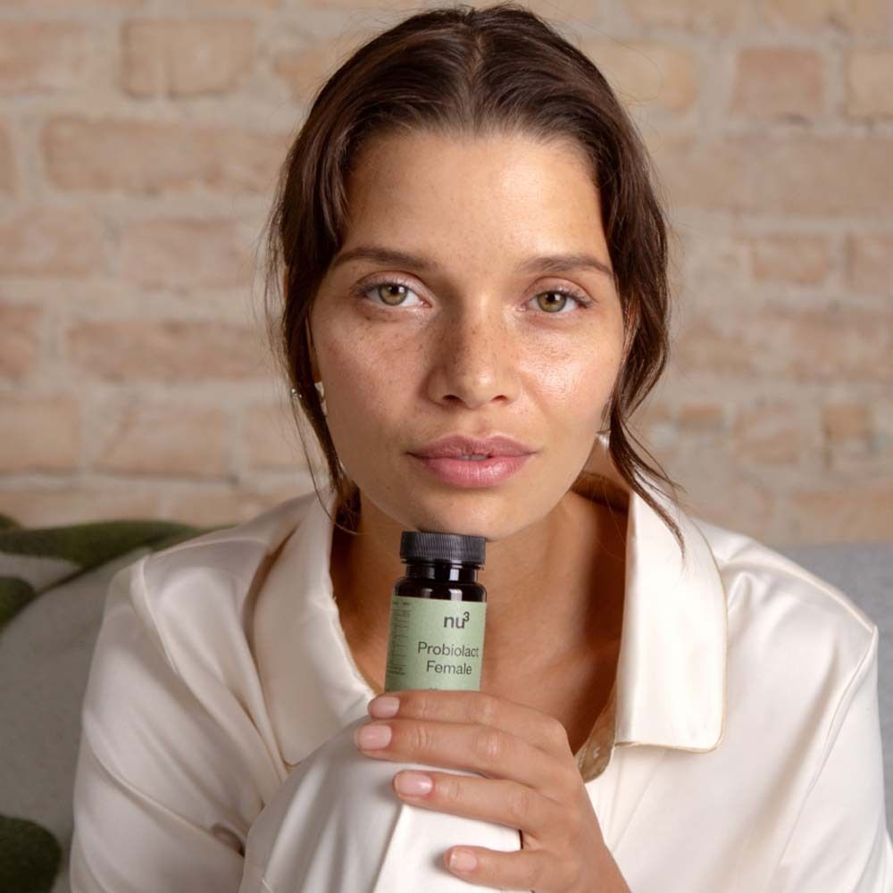 Femme tenant un flacon « nu3 Probiolact Female ». Flacon marron avec bouchon noir.