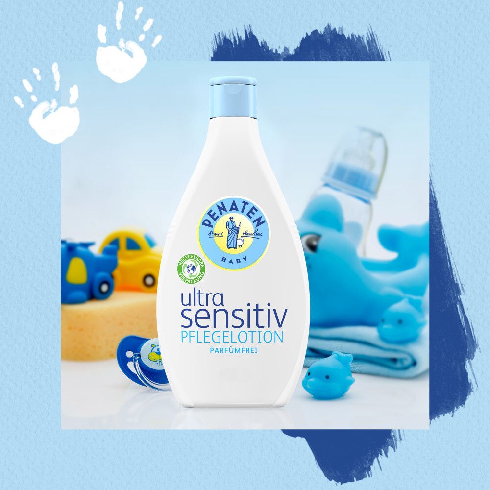 Weiße Flasche PENATEN® Ultra Sensitiv Pflegelotion. Auf blauem Hintergrund mit Spielzeug: Wal, Auto, Schnuller, Delfin.