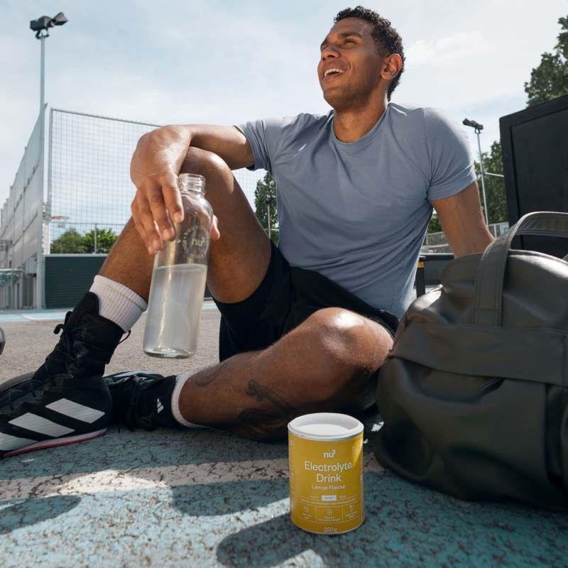 Mann sitzt nach dem Sport neben einer Dose nu3 Elektrolyte Drink Zitrone und einer Wasserflasche.
