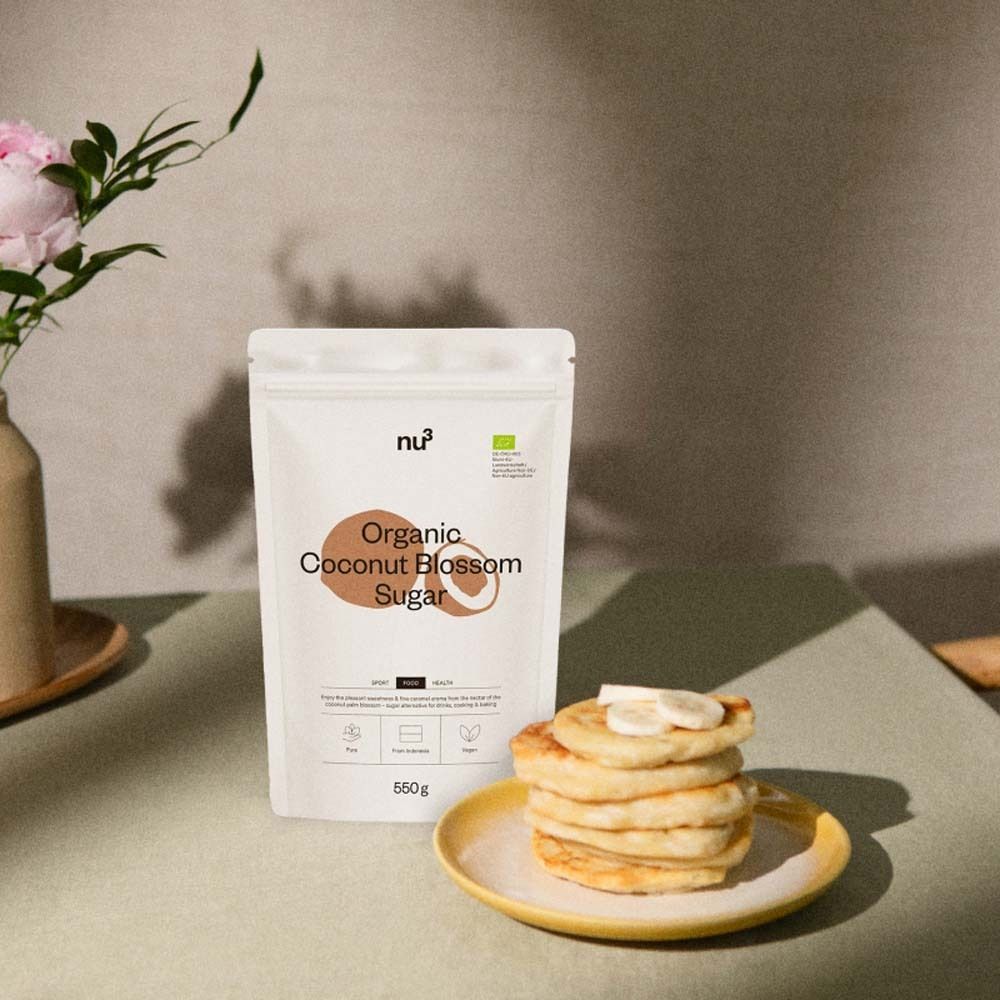 Emballage du produit à côté de crêpes sur une assiette jaune. Fleurs en vase. nu3 Organic Coconut Blossom Sugar, 550g.