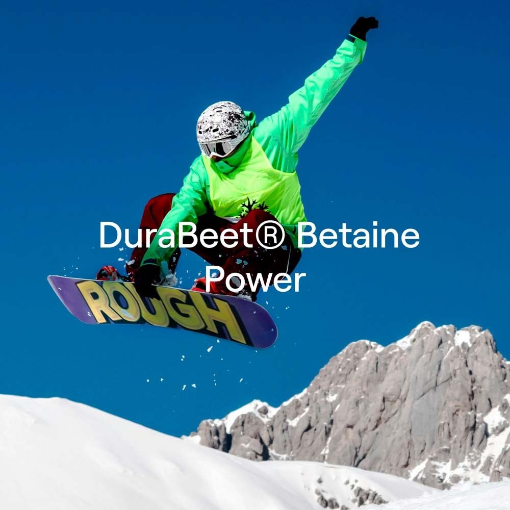 Snowboarder en l'air. Texte : "DuraBeet® Betaine Power". Montagne en arrière-plan. Ciel bleu.