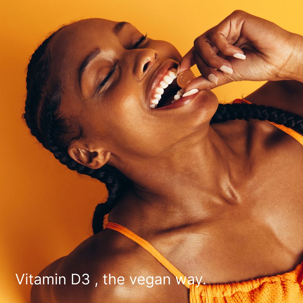 Frau isst Vitamin D Gummibärchen. Aufschrift: Vitamin D3, the vegan way.