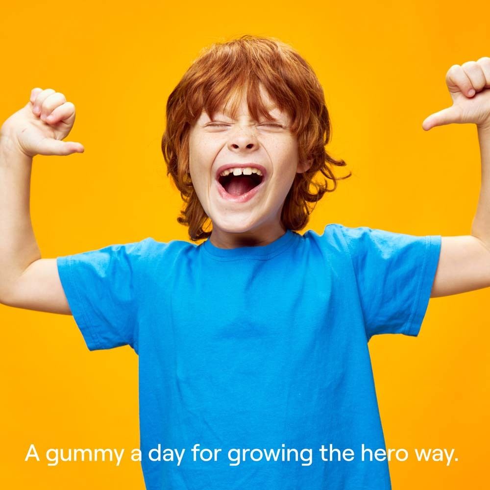 Un garçon en t-shirt bleu se montrant. Fond jaune. Texte : "A gummy a day for growing the hero way."