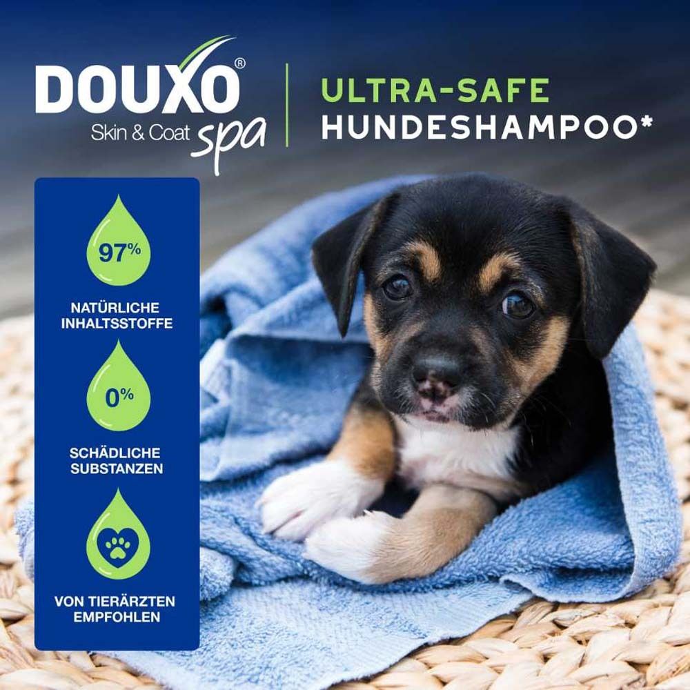 Schwarzer Welpe in blauem Handtuch. Text: DOUXO® Ultra-safe Hundeshampoo. 97% natürliche Inhaltsstoffe, 0% Schadstoffe.