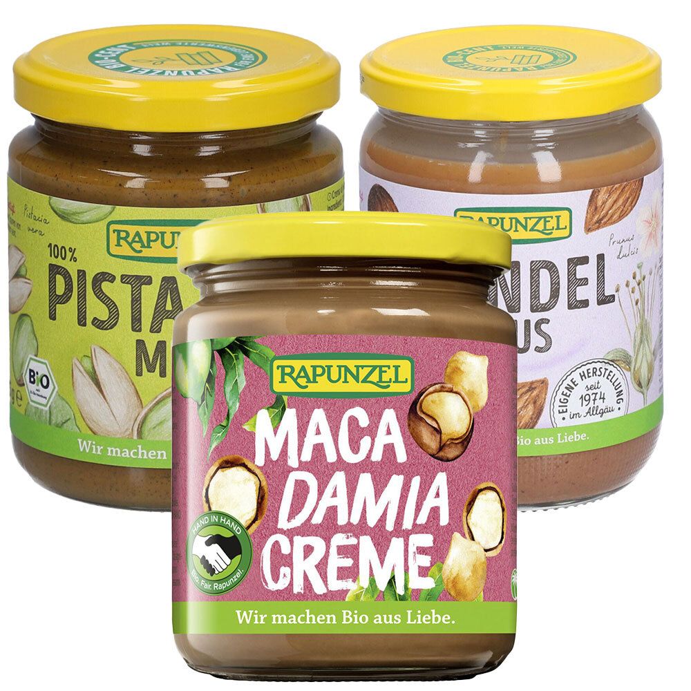 Trois pots de purée de noix. Étiquettes avec "Pistazienmus", "Mandelmus" et "Macadamia Creme". Couvercles jaunes. Marque : Rapunzel. Label bio.