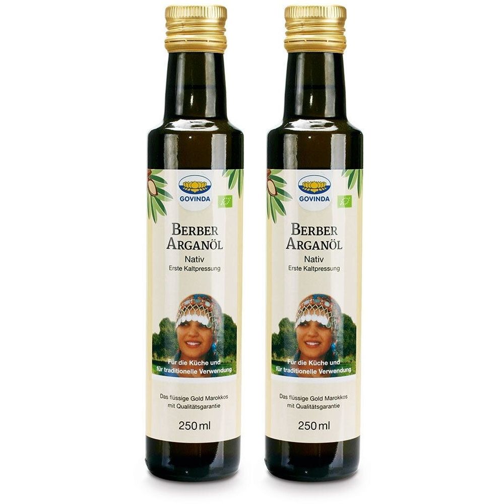 Deux bouteilles d'huile d'argan berbère. Bouteilles en verre foncé avec bouchons dorés. Étiquette avec nom du produit, visage de femme et label bio.