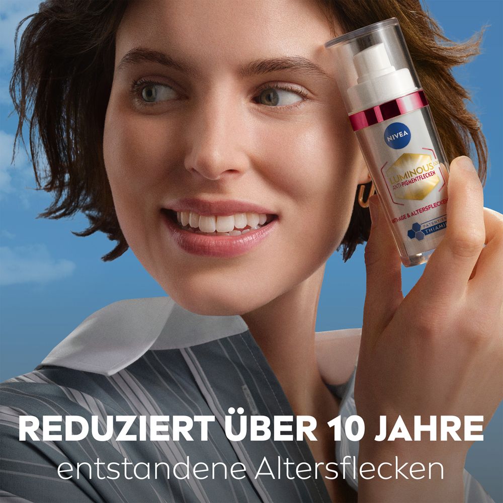 Frau hält Nivea Luminous 630 Anti-Aging Serum Flasche vor blauem Himmel.