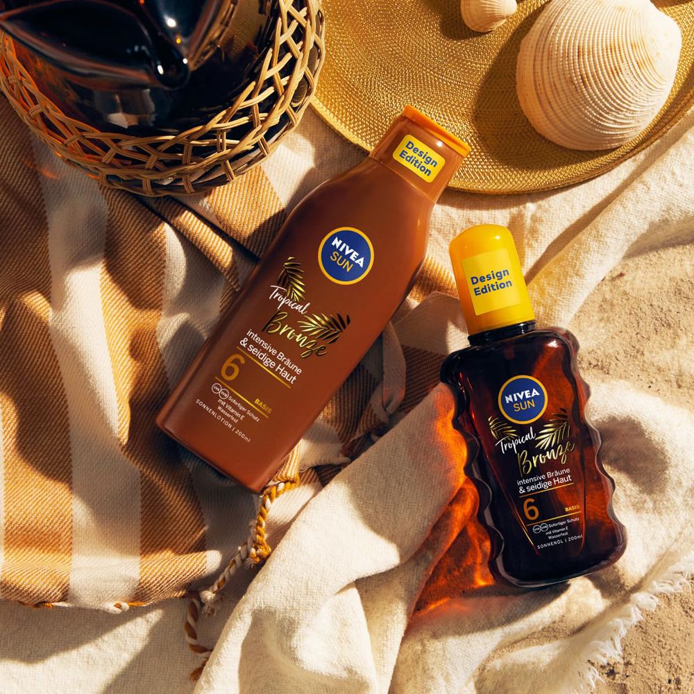 Zwei NIVEA SUN Tropical Bronze Flaschen, eine braune Lotion und eine braune Sprühflasche, auf einem Handtuch.