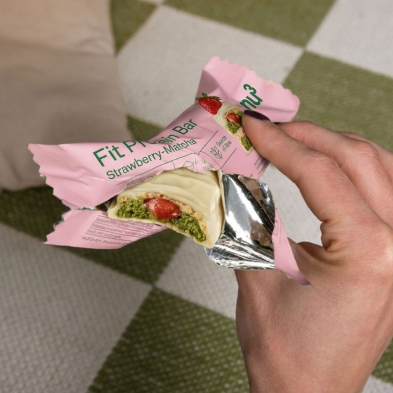 Une main ouvre l'emballage d'une barre protéinée nu3 Fit, Fraise-Matcha, révélant la barre.