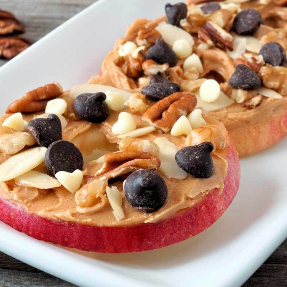 Zwei Apfelscheiben mit Mandelmus und Nüssen belegt.