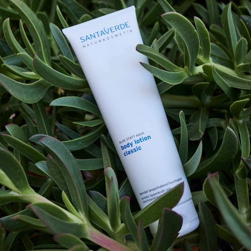 Tube blanche avec logo SANTAVERDE et inscription body lotion classic, posée sur des feuilles.