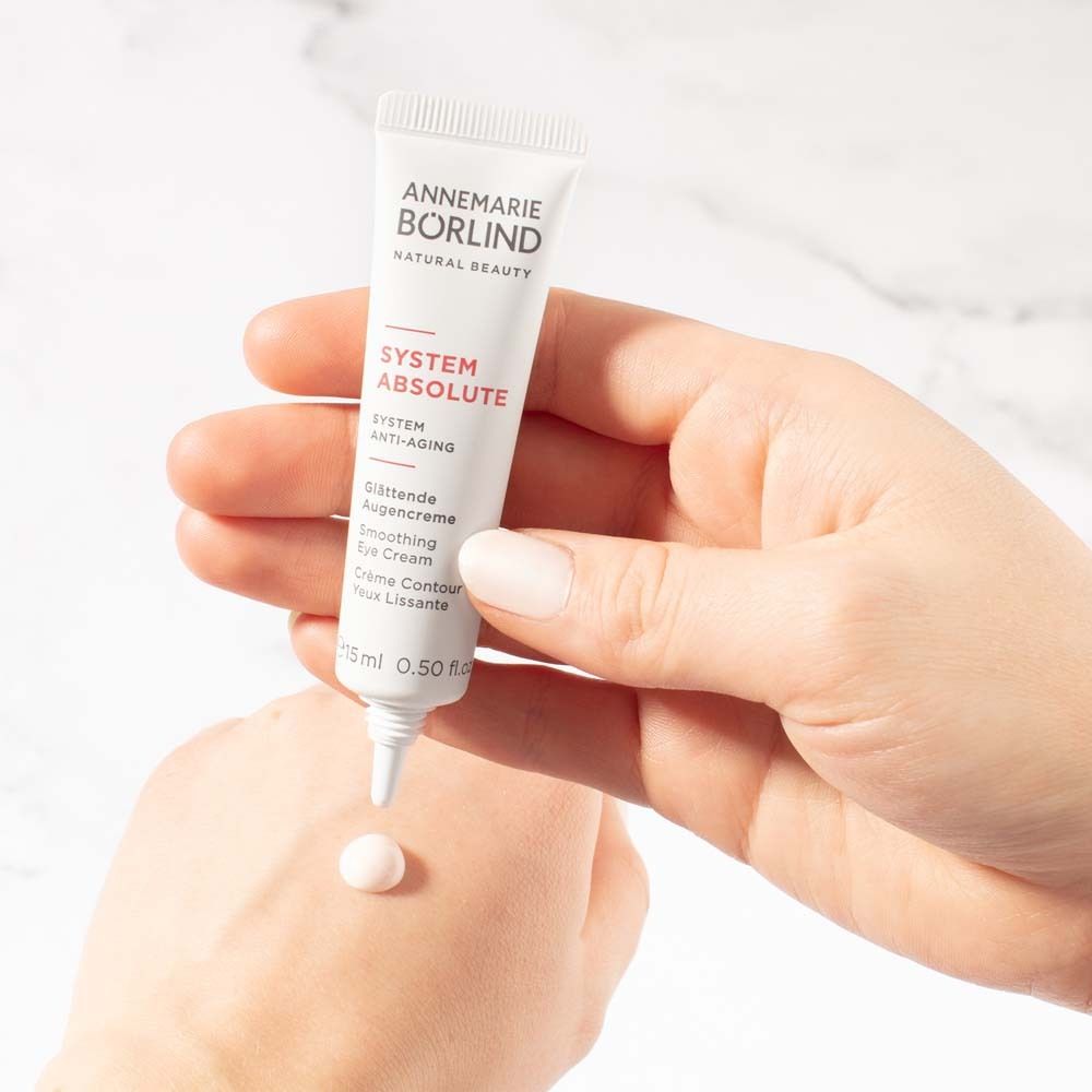 Tube de crème dans la main. Goutte de crème sur la main. Texte: ANNEMARIE BÖRLIND, SYSTEM ABSOLUTE, Crème Contour des Yeux Lissante.