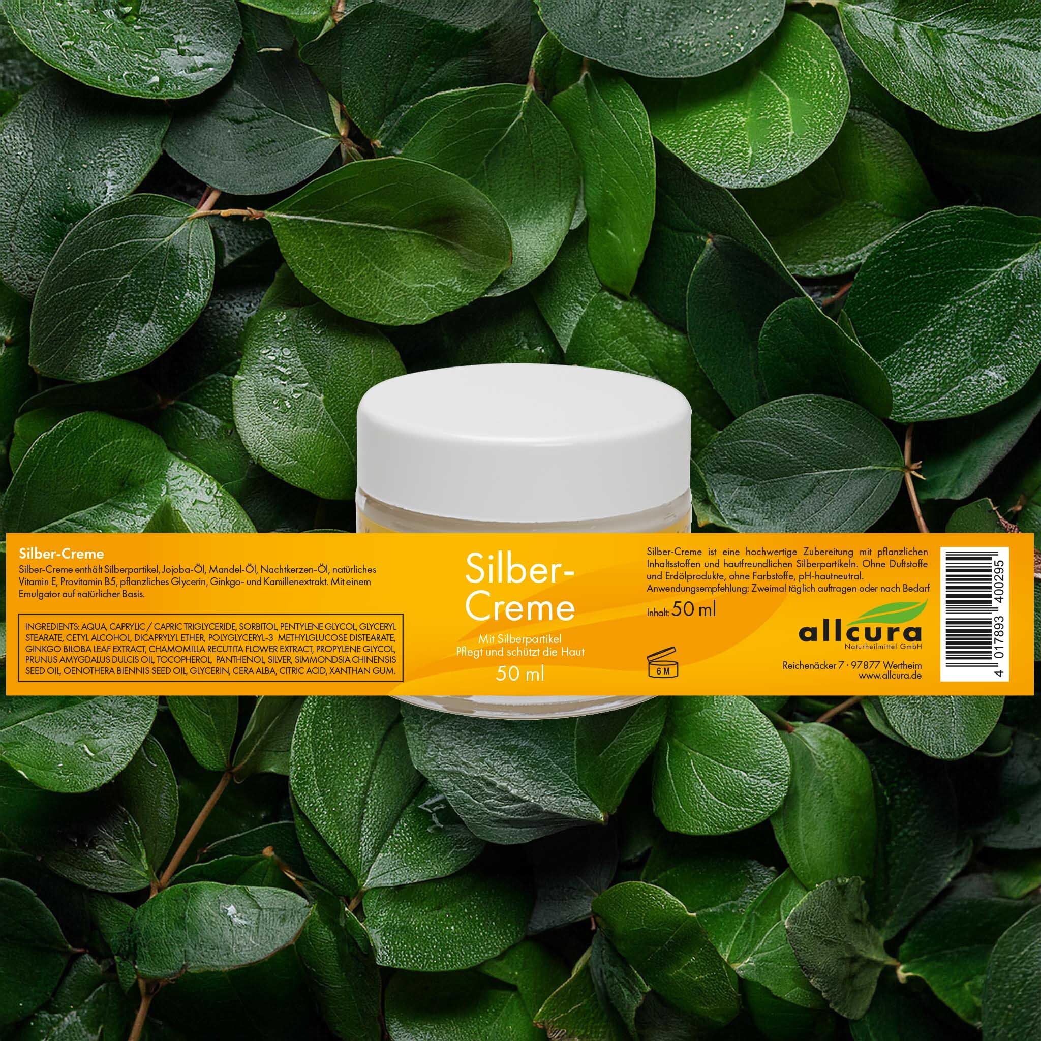 Pot en verre avec couvercle blanc, entouré de feuilles vertes. Étiquette jaune avec texte : Silber-Creme, 50 ml.