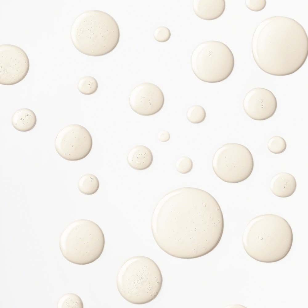 Petites gouttes rondes d'un liquide jaunâtre. Sur fond blanc. Aucune information sur le produit visible.