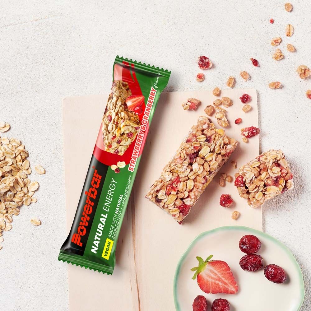 Powerbar Natural Energy Erdbeer-Cranberry Riegel, teilweise verzehrt, mit Früchten und Müsli auf Unterlage.