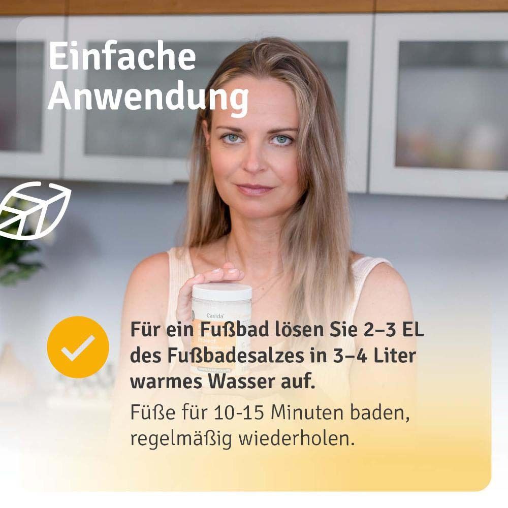 Femme tenant le produit. Produit : Casida Fußbadesalz Repair & Protect. Texte : Pour un bain de pieds, 2-3 CS dans 3-4 litres d'eau tiède.