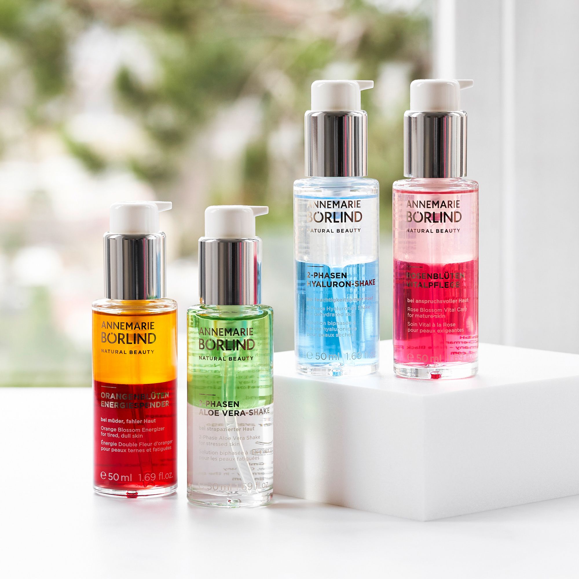 Vier ANNEMARIE BÖRLIND 2-Phasen Hyaluron-Shake Flaschen. Verschiedene Farben. Auf weißer Oberfläche.