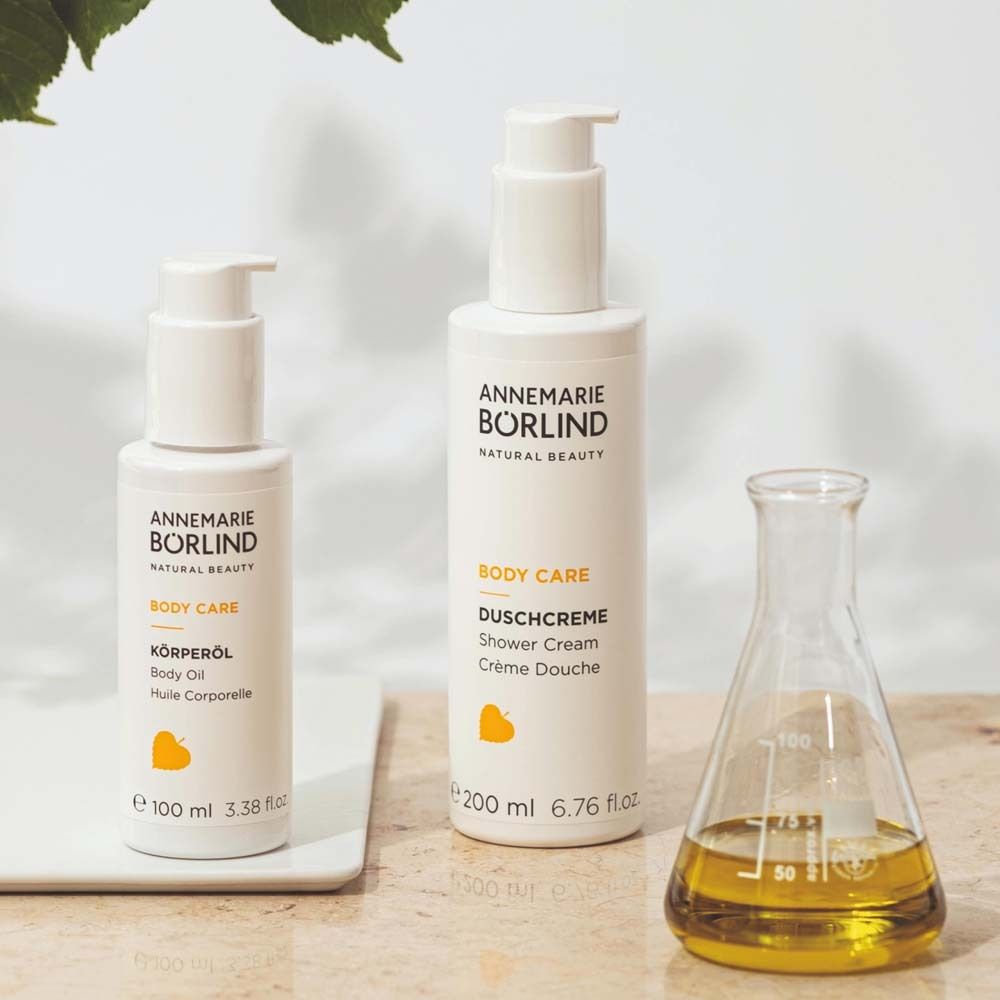 Zwei weiße Flaschen und ein Glasgefäß. Aufschrift: ANNEMARIE BÖRLIND, BODY CARE, KÖRPERÖL, DUSCHCREME. Gelbes Logo.