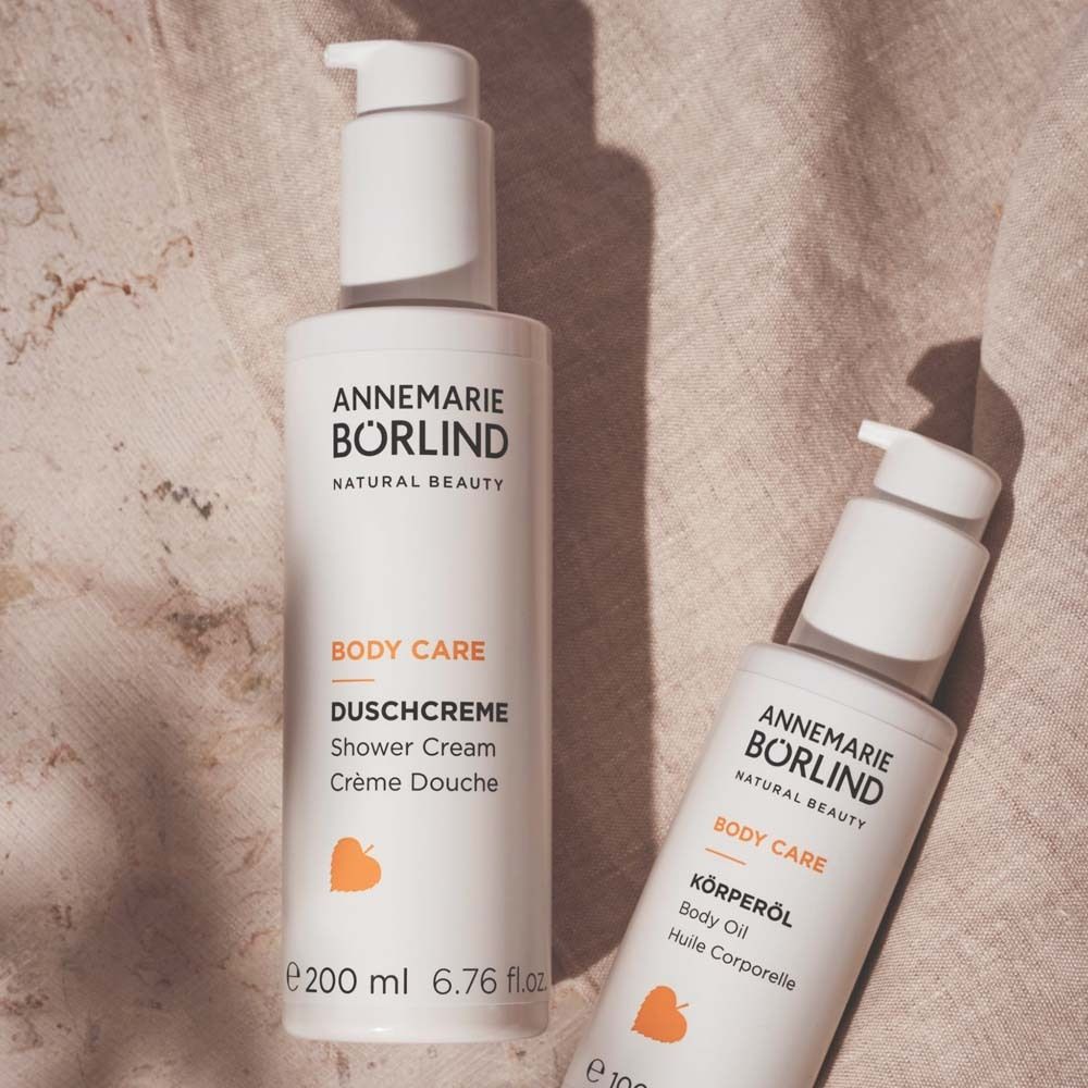 Zwei weiße Flaschen mit Pumpverschluss. Aufschrift: ANNEMARIE BÖRLIND, BODY CARE, KÖRPERÖL, DUSCHCREME. Gelbes Logo.