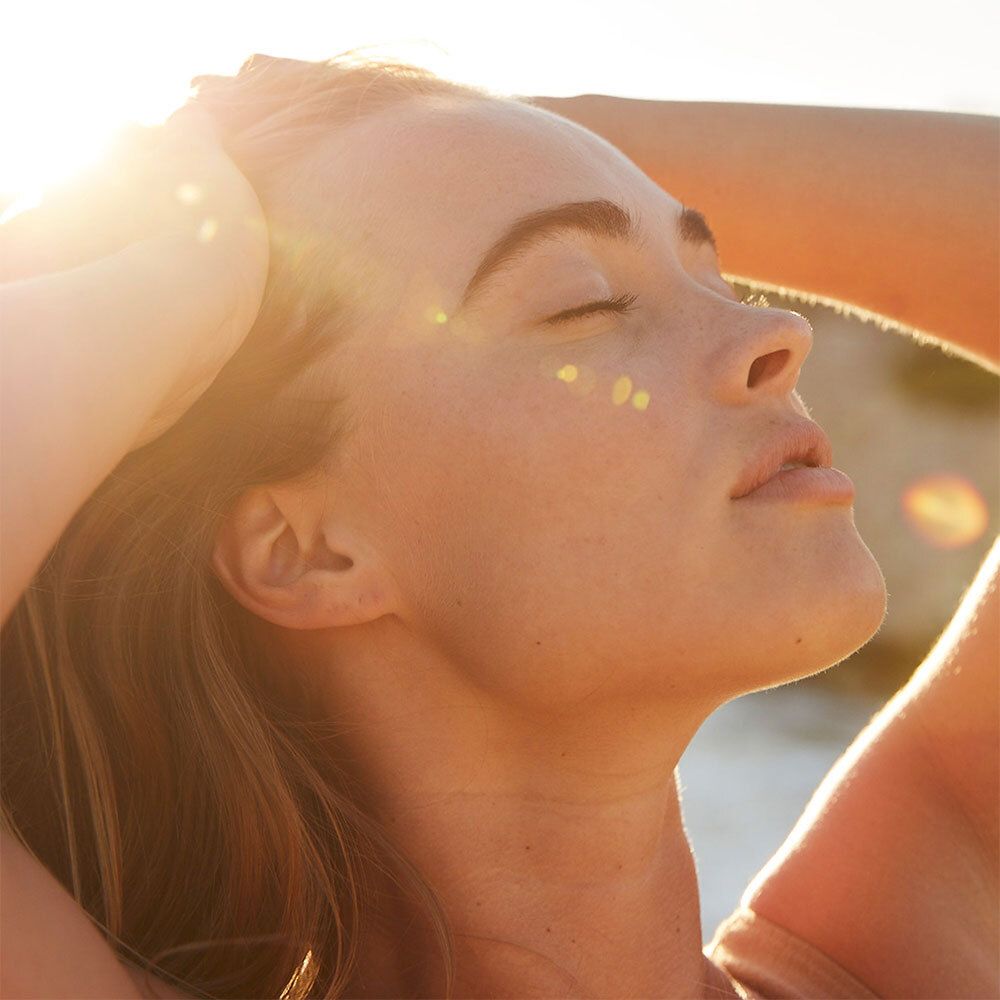 Une femme aux yeux fermés, le visage tourné vers le soleil. Ses cheveux sont légèrement ondulés.