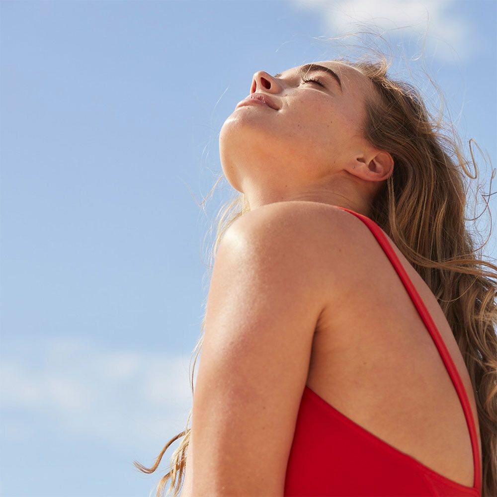 Une femme en maillot de bain rouge inclinant la tête vers le ciel. Ses cheveux sont ondulés.