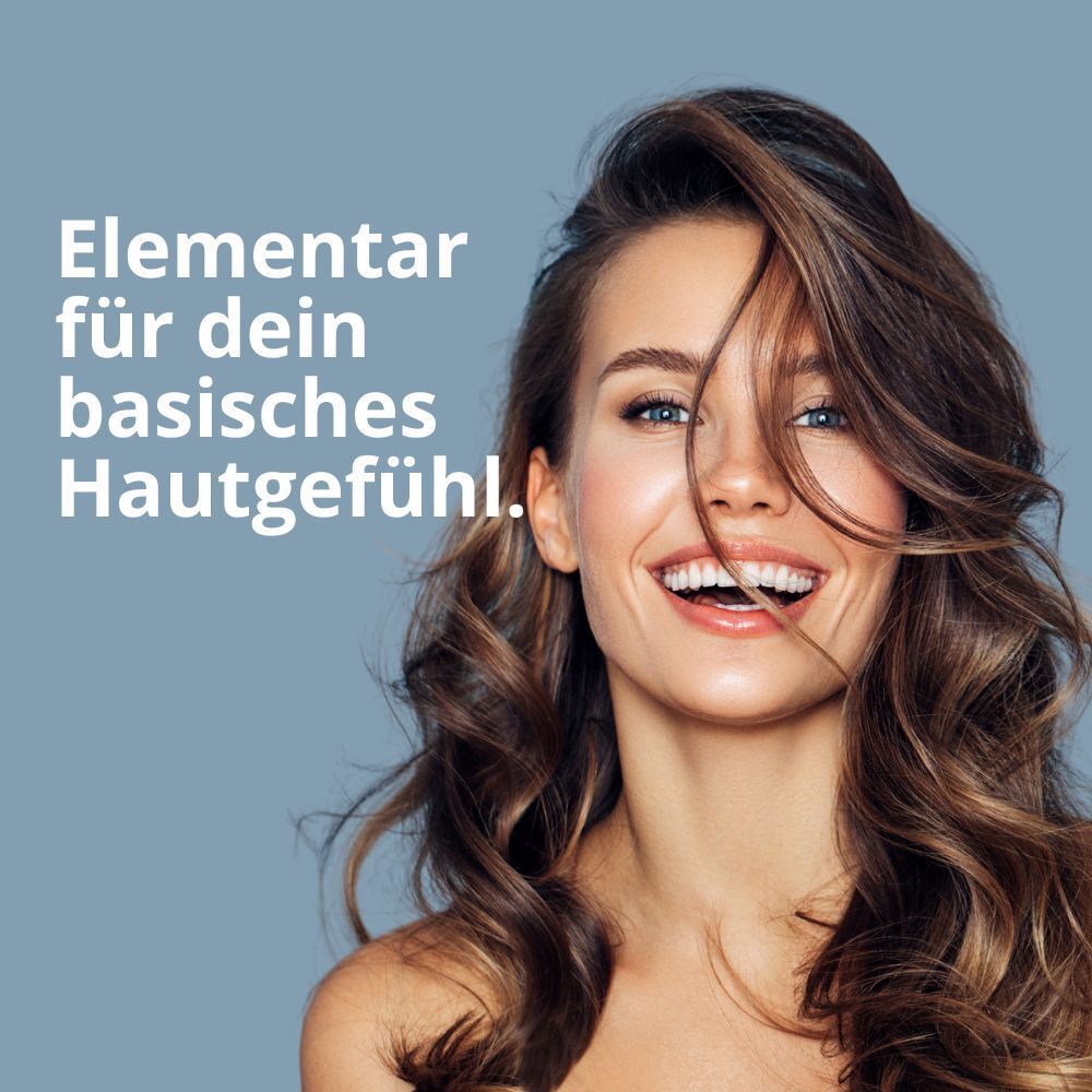 Frau mit langen, braunen Haaren lächelt. Text: Elementar für dein basisches Hautgefühl.
