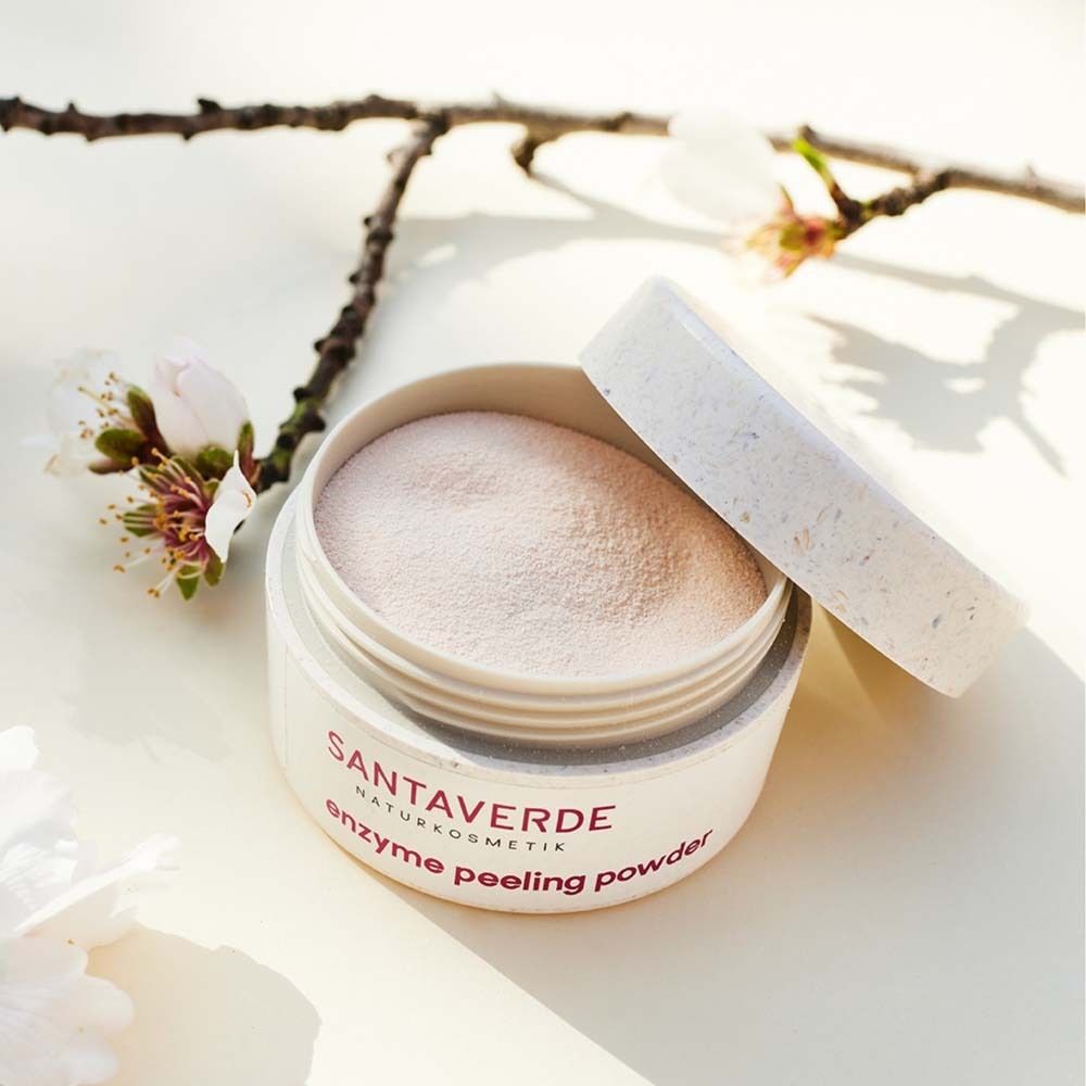 Pot ouvert avec SANTAVERDE enzyme peeling powder. Poudre rose visible. Branche fleurie en arrière-plan.